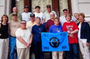Vietnam veterans and their wives at a reunion holding a blue flag