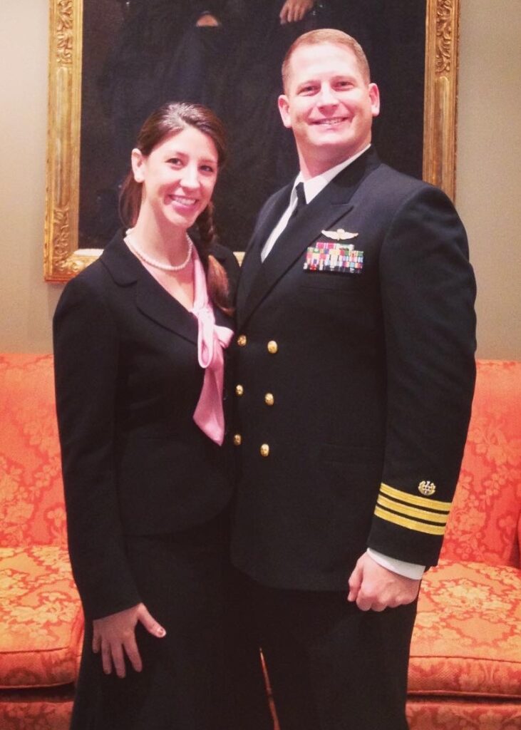 A Navy Commander in his dress blue uniform standing with his wife