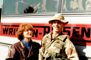 A red-haired woman standing next to a U.S. Army soldier in front of a bus.