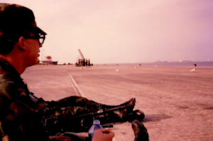 A U.S. Army soldier drinking bottled water looking out at a vast stretch of sand at the port of Jubail in Saudi Arabia