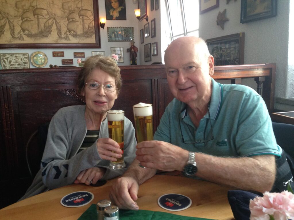 Husband and wife in a bar each holding a tall glass of beer.