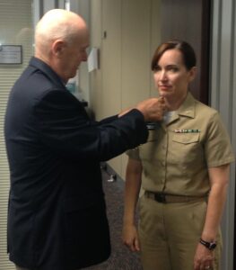 A man pinning the rank insignia on the collar of a female Navy officer's uniform