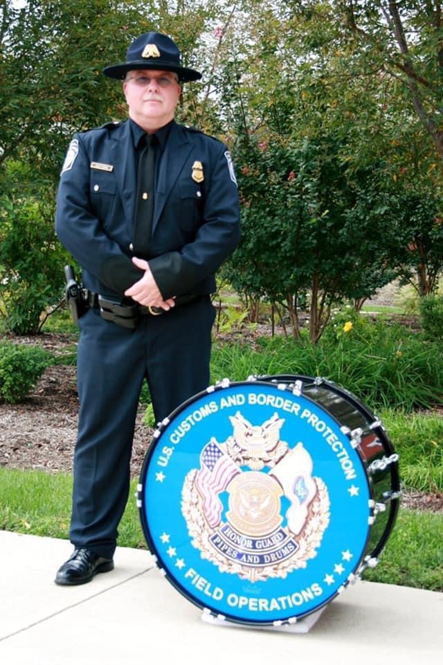 Man wearing a U.S. Customs and Border Protection uniform standing next to a bass drum