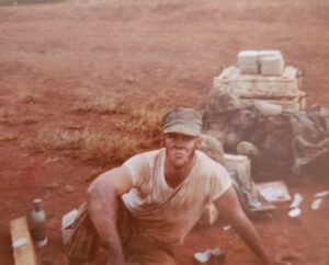 A Marine smudged with dirt sitting next to his equipment in the field.