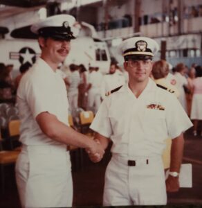 Navy airman shaking hands with a Navy lieutenant both wearing summer white uniforms