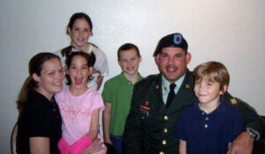 A husband wearing an Army uniform with his wife and their four children