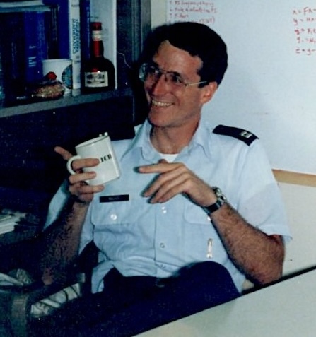 Male Air Force captain sitting down while holding a coffee cup and smiling