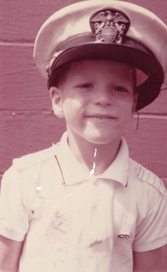 Young boy wearing an adult's Navy officer's uniform hat