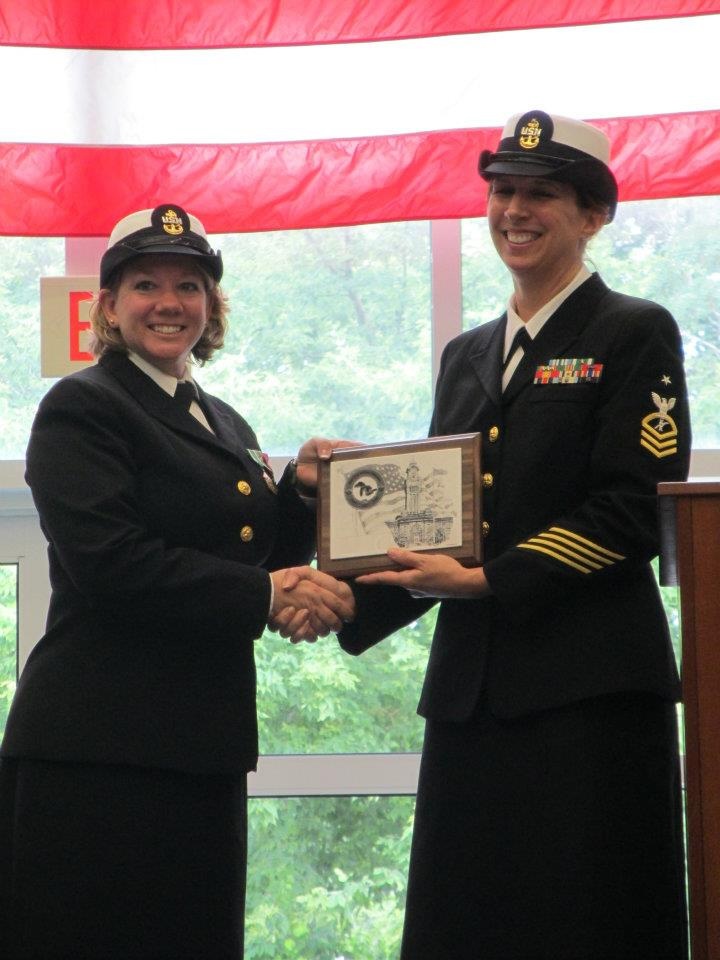 A female chief petty officer jointly holding a plaque with a female senior chief petty officer