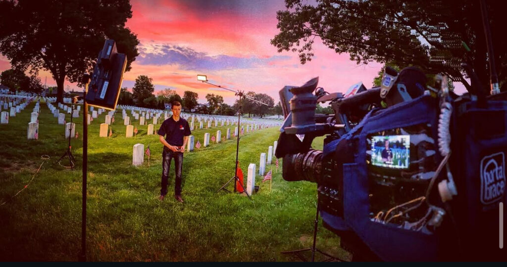 Male reporter doing a broadcast on camera in a National Cemetery.
