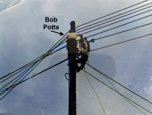 Two Marines installing wires at the top of a telephone pole
