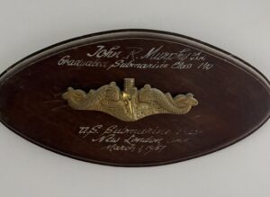 Oval plaque with golden submarine dolphin insignia in center.