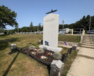 Granite stone memorial with silhouette of submarine on top and flowers planted at base