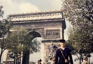 U.S. Navy sailor in winter blue uniform standing in front of the Arc de Triomphe