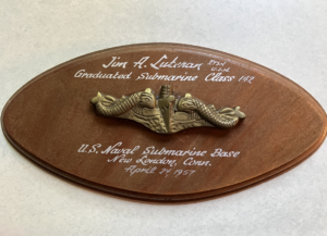 An oval wood Submarine School plaque with a dolphin badge and painted text